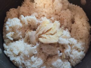 Partially cooked glutinous rice simmering with fresh ginger slices in a cooking pot before being wrapped in banana leaves for traditional Filipino suman.