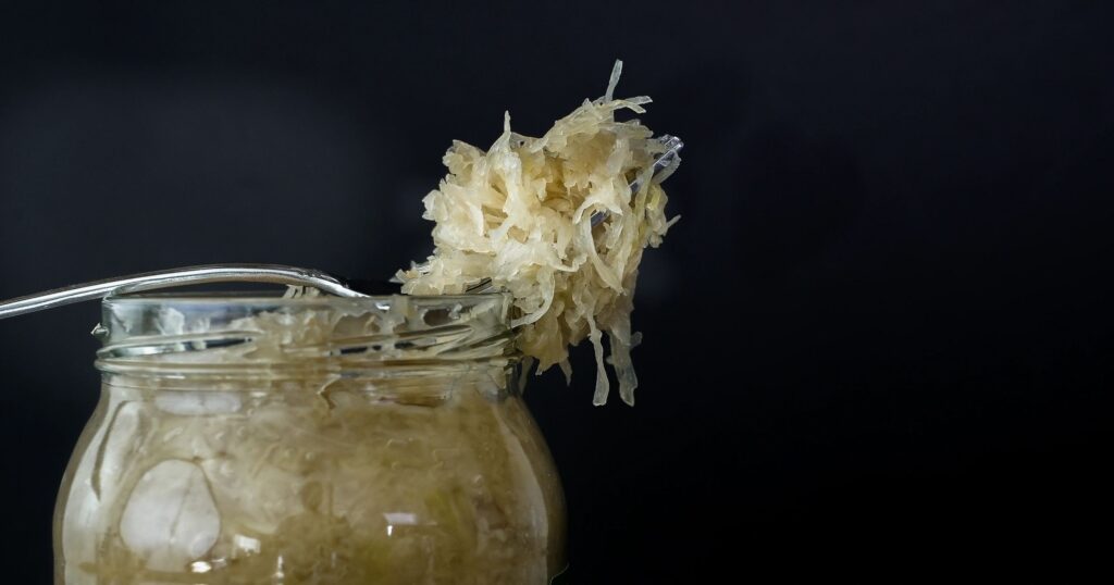 Homemade sauerkraut in a jar with a fork lifting fermented cabbage